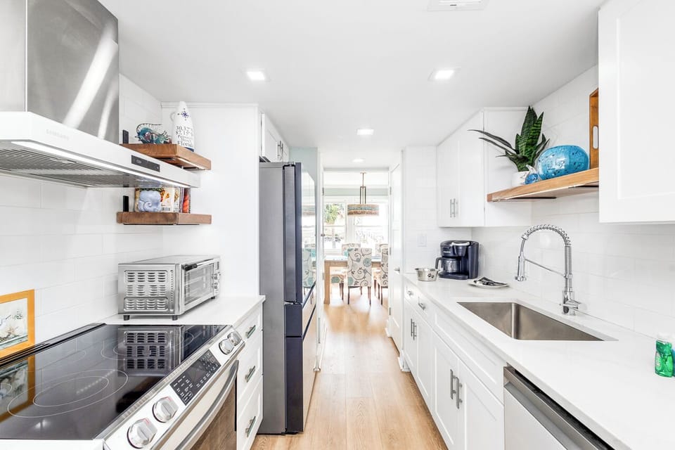 Prepare delicious meals in your bright, fully-equipped galley kitchen with modern appliances, sleek white cabinets, and thoughtful touches like fresh plants.