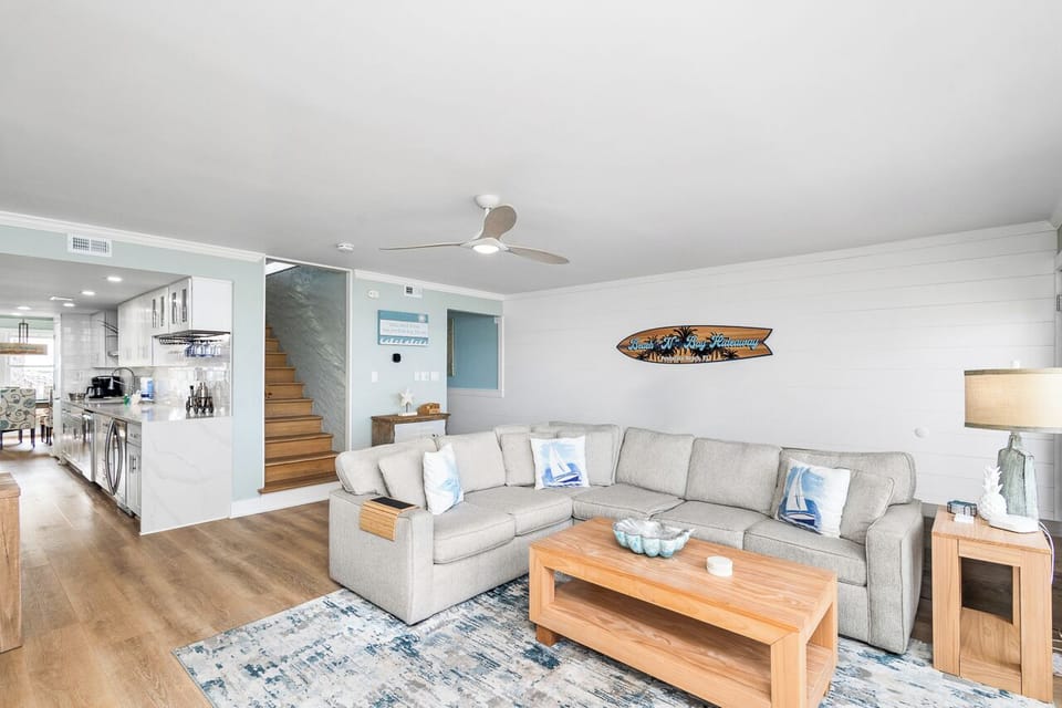 Relax in your spacious living room featuring a plush sectional sofa, coastal décor, and seamless flow to the modern kitchen.
