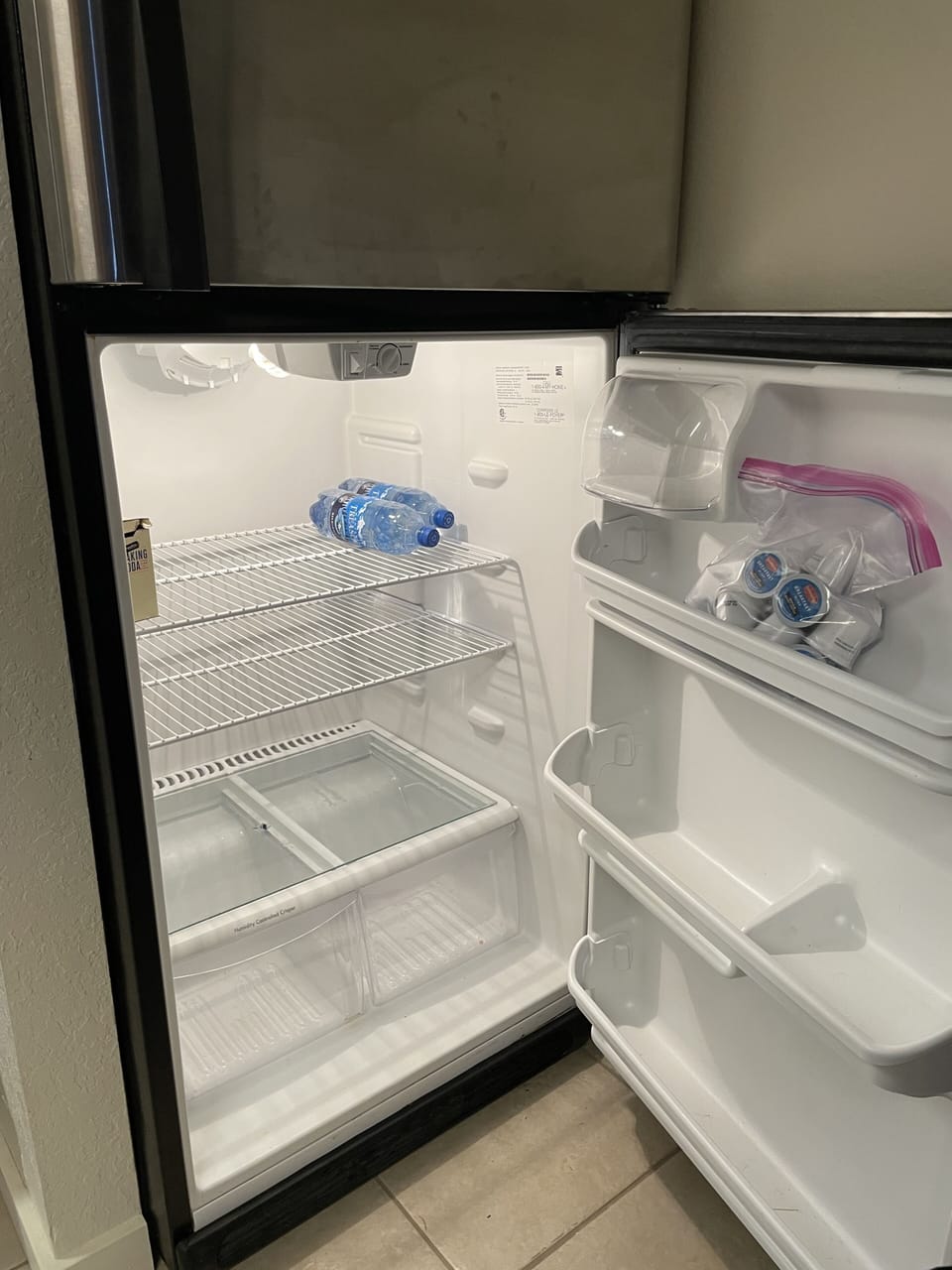 Clean refrigerator/freezer with extra coffee pods and bottled water. 