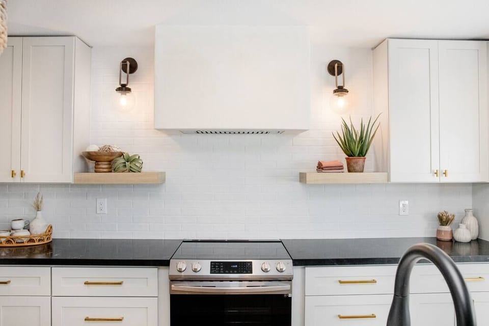Modern kitchen with black countertops and white cabinetry featuring brass hardware.