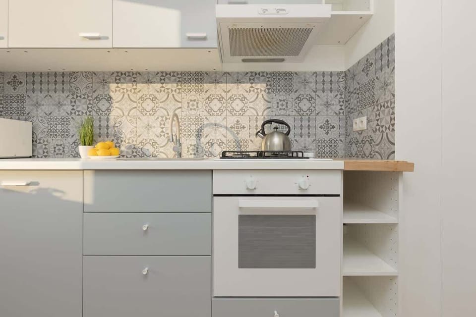 A close-up of a modern kitchen with grey cabinets, a tiled backsplash, and an oven. A bowl of lemons adds a decorative touch.
