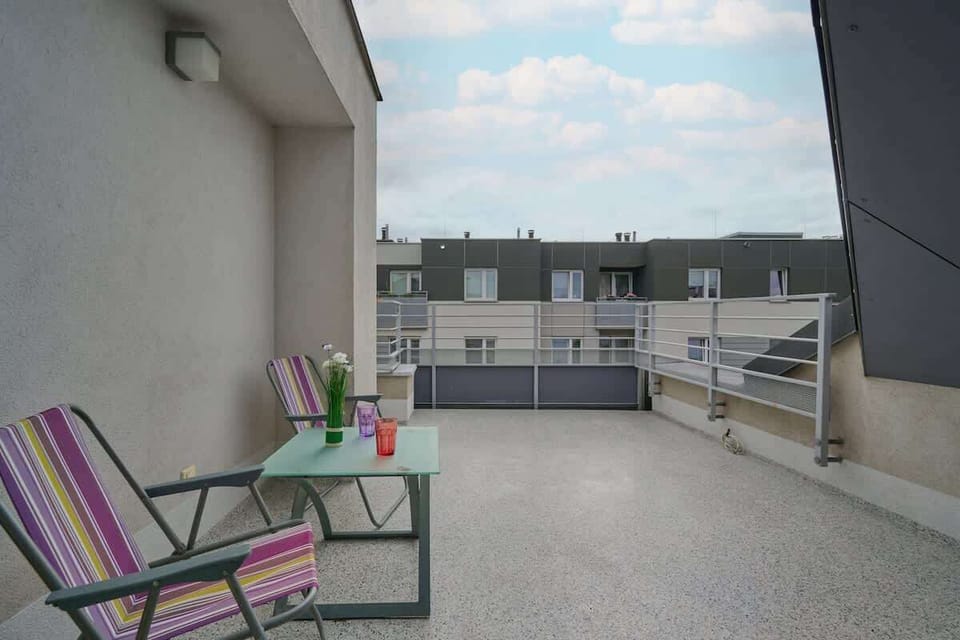 A spacious balcony with outdoor chairs and a small table, offering a relaxing space with a view of the surrounding buildings.
