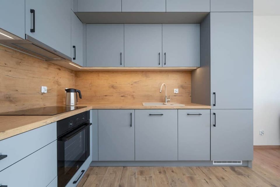 A modern kitchen with grey cabinets, a wooden backsplash, and sleek appliances, designed for functionality and style.
