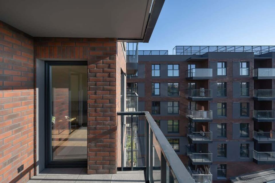 A balcony view, showcasing a red brick exterior and a view of the modern residential area.
