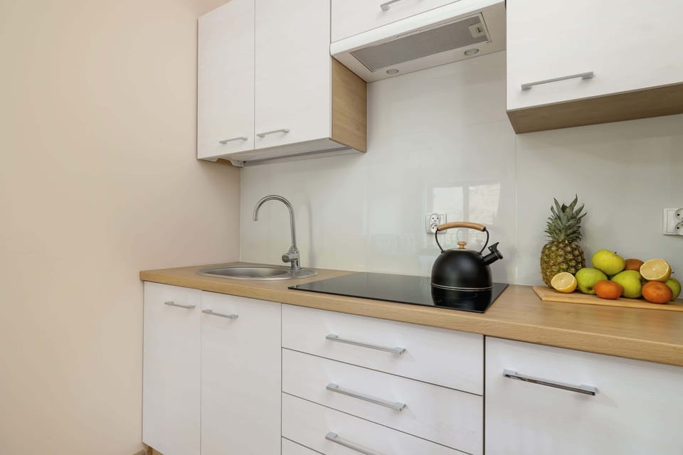 A modern kitchen with white cabinets, a sleek countertop, and small decorative touches like fruits and potted plants.
