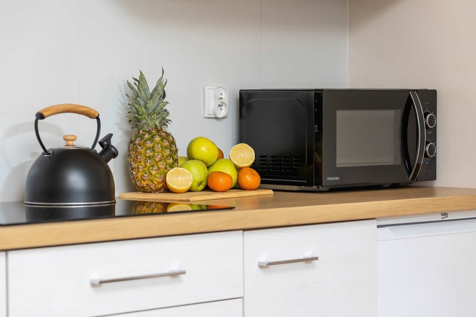 A close-up of a modern kitchen counter, featuring a microwave, a black kettle, and fresh fruits for a vibrant and functional design.
