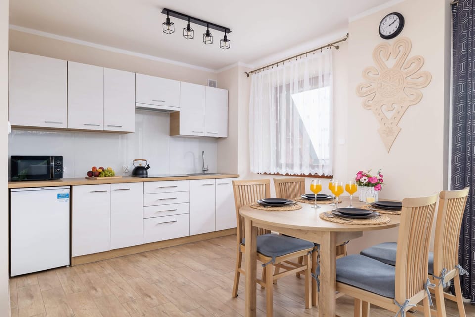 A modern kitchen and dining area featuring sleek white cabinetry, a wooden table, and bright natural light.

