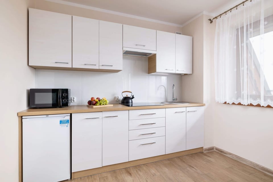 A compact kitchen with white cabinets, modern appliances, and a window providing plenty of natural light.
