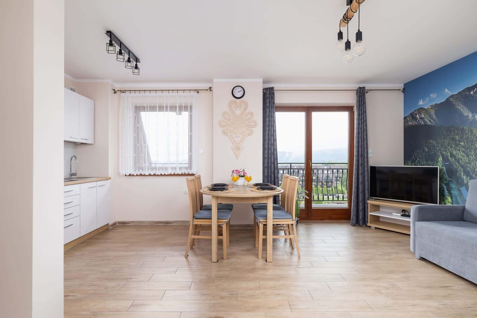 A view of the open-plan kitchen and dining area, featuring modern furniture, a wooden floor, and access to a balcony with mountain views.
