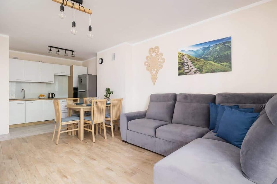 A combined view of a living and dining area, with a gray sofa, a table, and a glimpse of a modern kitchen.