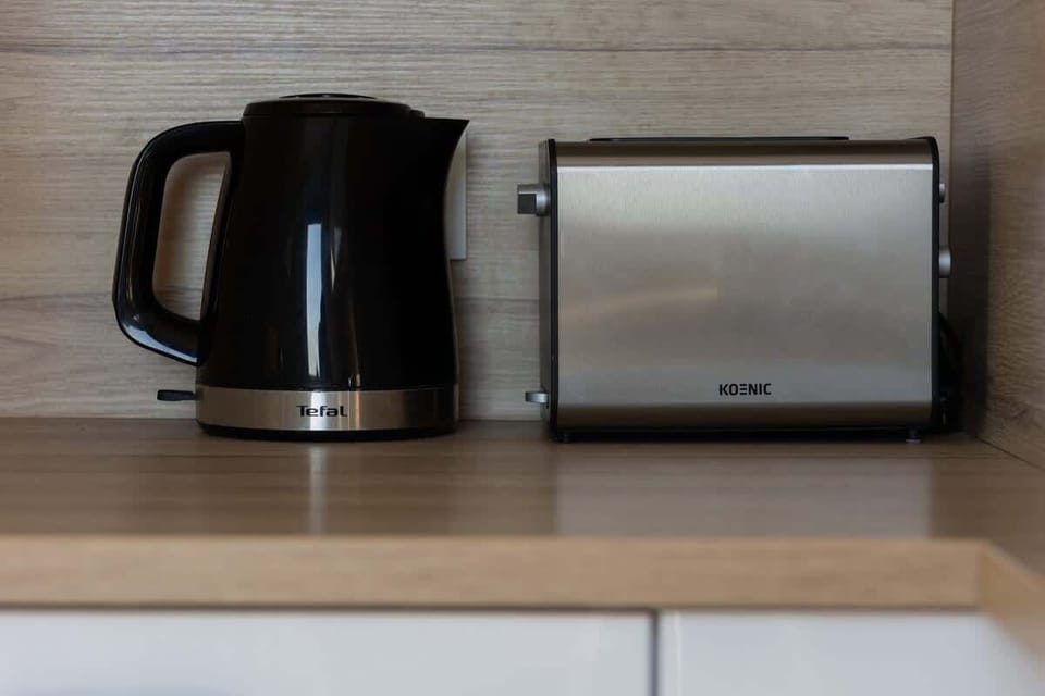 A kitchenette corner with a black kettle and a silver toaster on a wooden countertop, combining functionality with simplicity.
