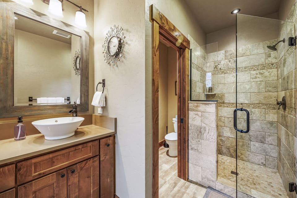 En suite of this mountain sanctuary, boasting a stunning stone shower, heated tile floors, and a modern vessel-mounted sink