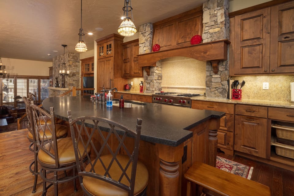 - Gourmet kitchen with stone insets and dark countertops brings stylish lodge vibes - Large island with seating perfect for breakfast spreads or après ski drinks - Pendant lighting and red accents add warmth and a cozy mountain glow