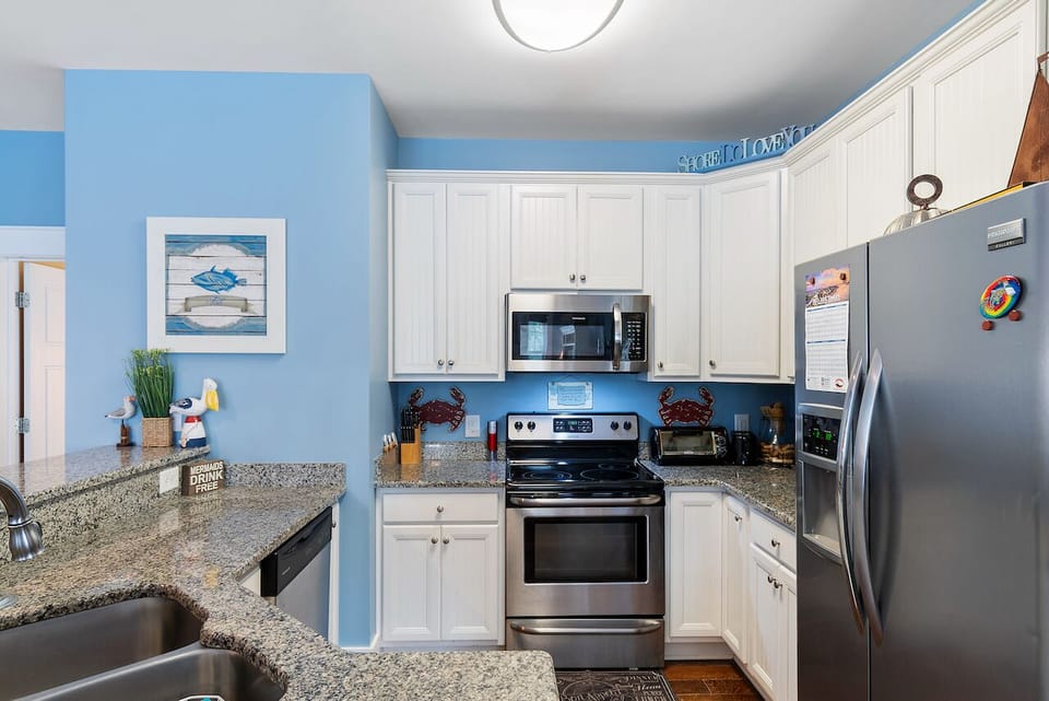 Your bright coastal kitchen awaits with granite counters, stainless appliances, and cheerful blue walls that bring beachy vibes to every meal.