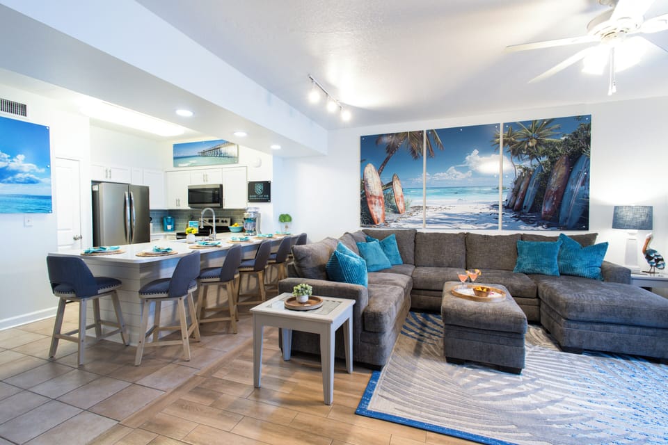 Open-concept living area with a sectional sofa and coastal-themed artwork.