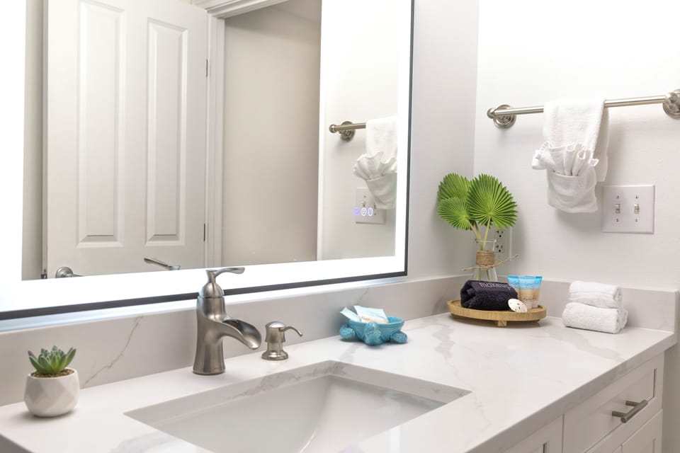 Modern bathroom sink area with a large illuminated mirror and neatly arranged toiletries.
