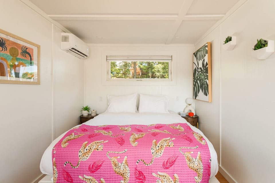 Queen Helix Luxe bed dressed in Parachute linens with a vibrant cheetah throw, framed by tropical-inspired Boho artwork and a window onto the Magothy treetops.