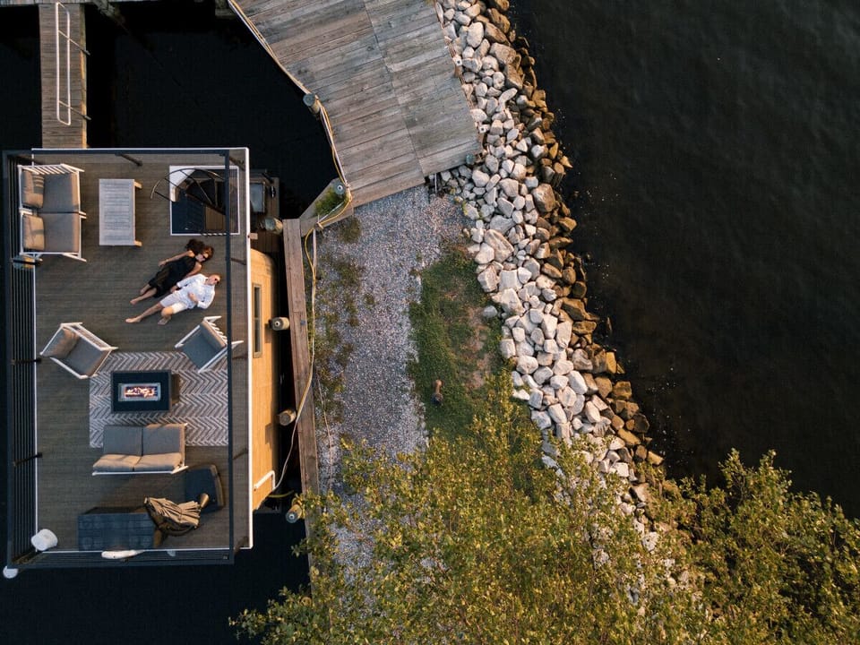 Aerial view of Bung-a-flo at golden hour, with guests relaxing on the rooftop deck framed by the rocky shoreline of the Magothy River.