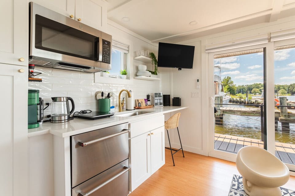 Compact galley kitchen with a Keurig, electric kettle, single-seat bar, mounted Roku Smart TV, and sliding glass doors opening to the marina and Magothy River.