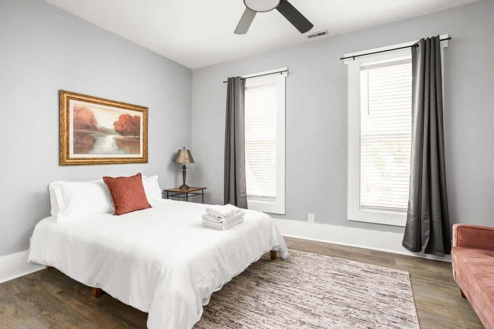 The bedroom's charm with a great window allowing natural light, complemented by a bedside table and lamp, a dresser for storage, and the added comfort of a futon.