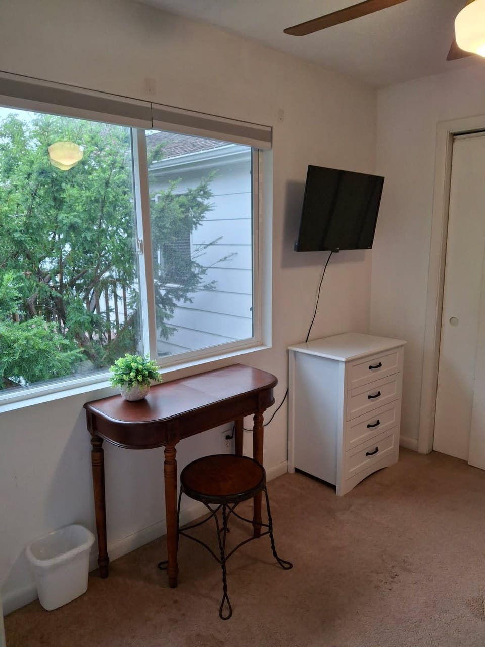 Bright bedroom nook with leafy views, desk, TV, and extra storage