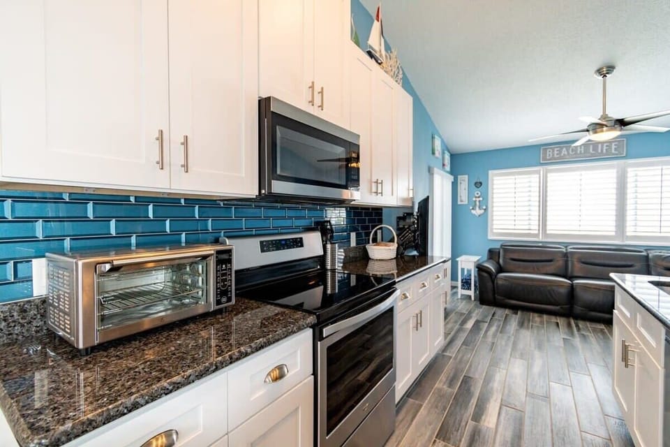 Modern kitchen with stainless steel appliances and blue tile backsplash overlooking a cozy living area.