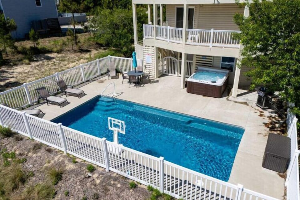 Aerial view reveals the property's impressive outdoor amenities: a private pool, elevated decks, and hot tub nestled among coastal greenery—your perfect vacation retreat.