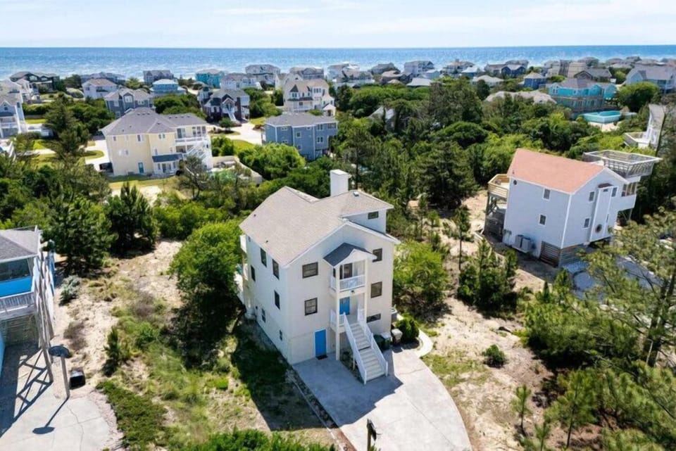 Elevated view of a coastal community showcasing the property's peaceful location near sandy shores, surrounded by mature trees and neighboring beach homes.