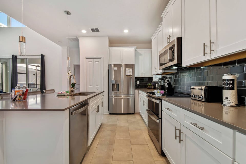 Welcome to a modern kitchen with sleek stainless steel appliances and a spacious island, ideal for meal prep or casual dining. The combination of white cabinetry and dark countertops offers a stylish and inviting atmosphere.