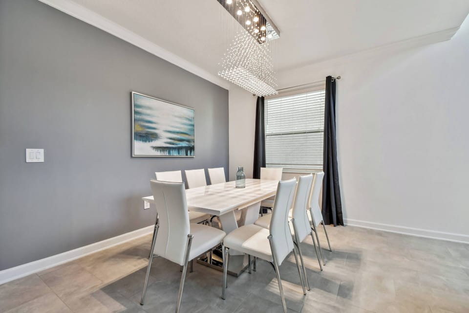 Bathe in natural light as you gather around the sleek, modern dining table, complemented by stylish white chairs. The soft gray walls and contemporary artwork create a calm atmosphere, making every meal a delightful experience.