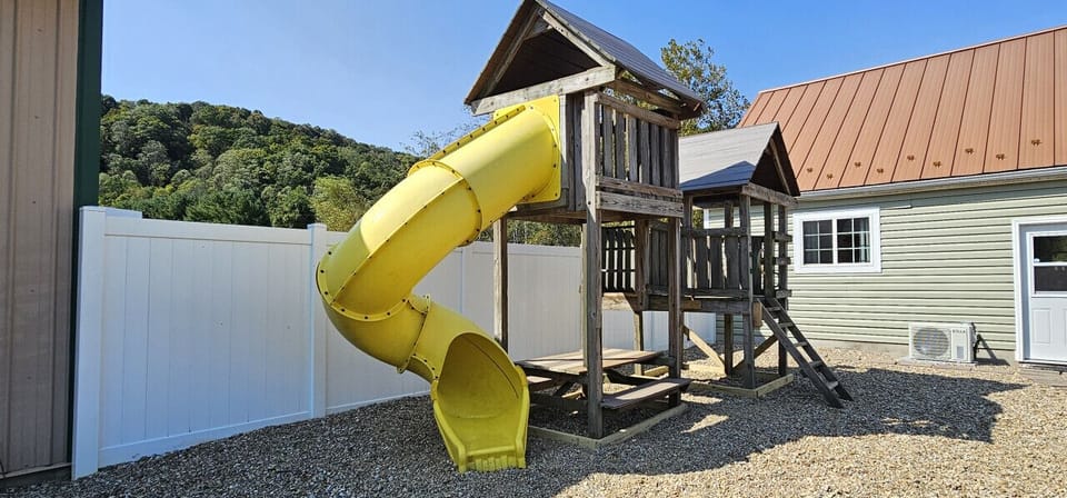 Kids will love this wooden playset featuring a bright yellow slide and a built-in, kid-sized picnic table. Conveniently located in the backyard, it offers a perfect space for fun with beautiful hillside views.