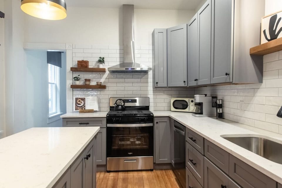 Modern kitchen with gray cabinets, a white island, stainless steel appliances and pendant lighting