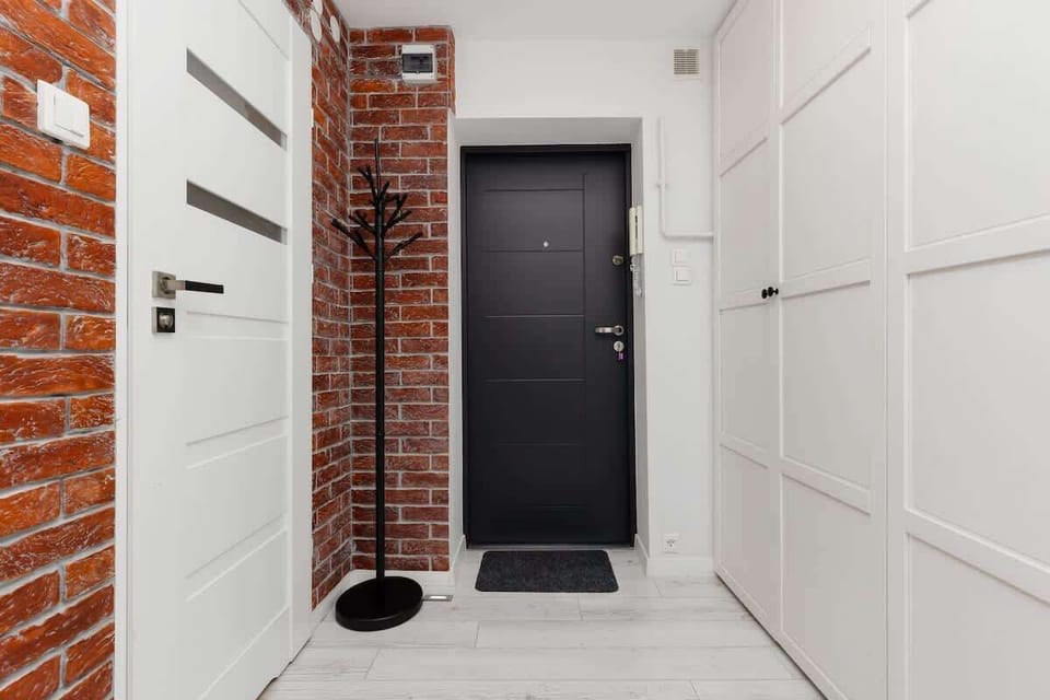 A hallway with a black front door, white walls, and a touch of exposed brick, blending industrial and modern styles.
