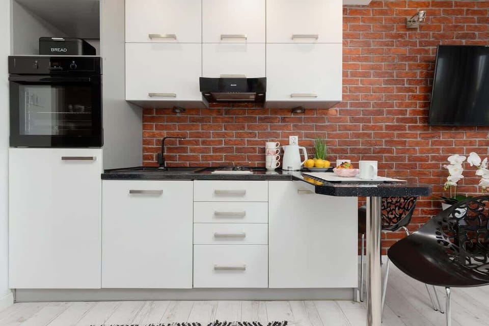 A modern kitchen with white cabinetry, a black countertop, and a striking brick accent wall for contrast.
