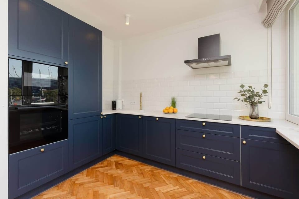 A kitchen with dark blue lower cabinets and white upper cabinets. It features a clean, modern design, with white tiled walls and sleek appliances.