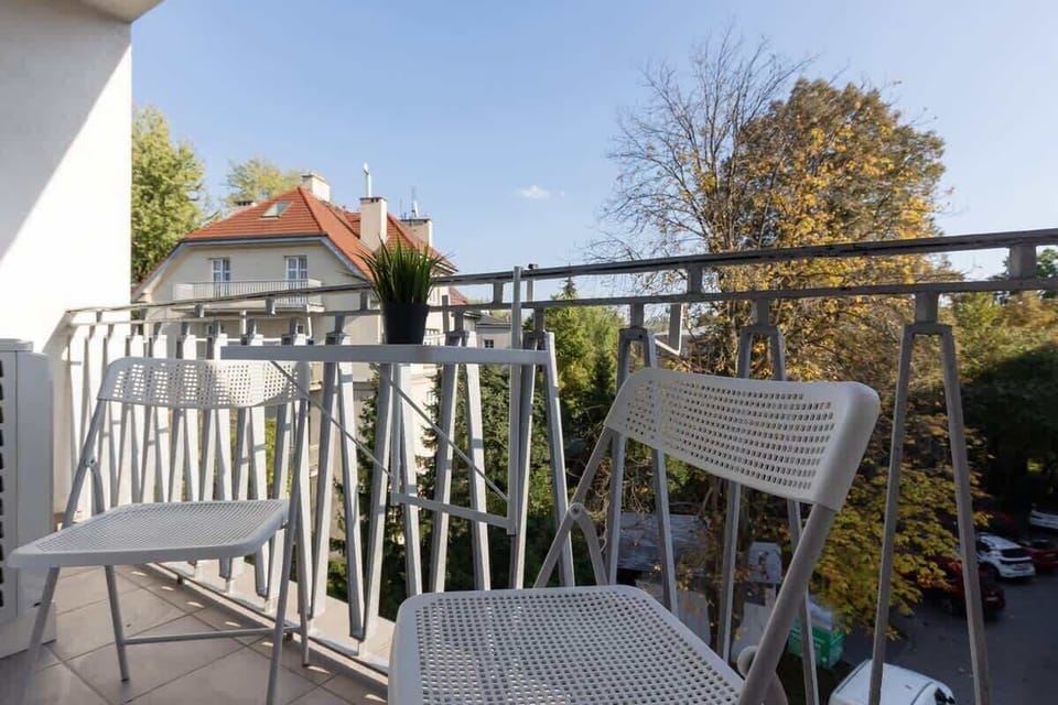 A balcony with a small table and two chairs. It offers a view of the trees and surrounding buildings, providing a nice outdoor spot for relaxing.