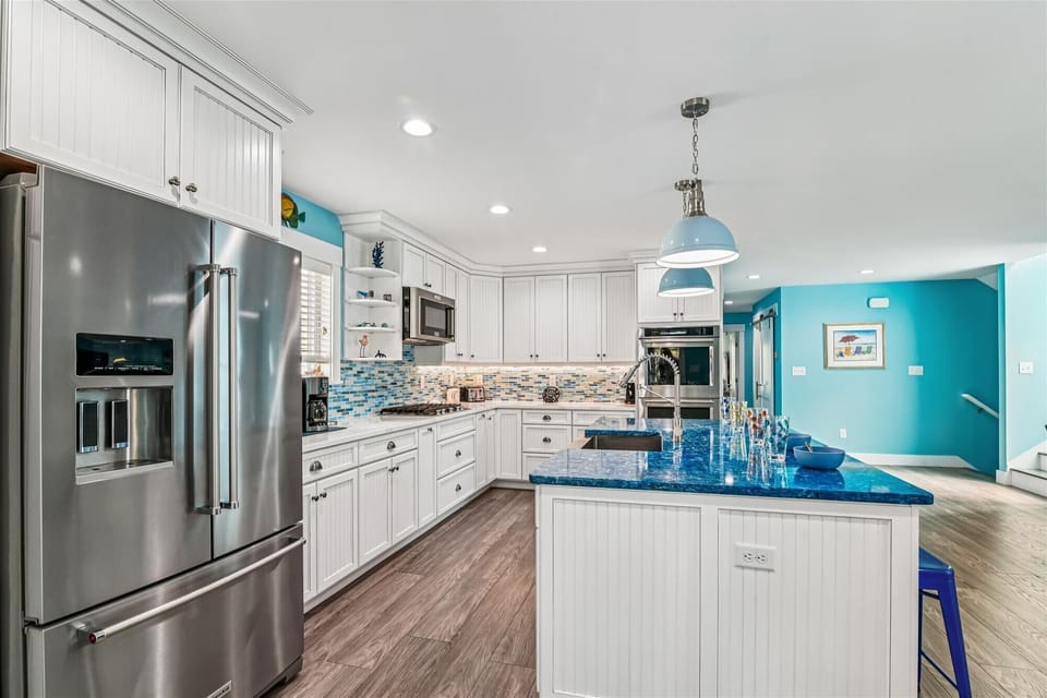 646 Tingle Ave - Modern Culinary Suite - Highlighting the kitchen's functionality, this view showcases the built-in oven, large refrigerator, and ample counter space. The subway tile backsplash and recessed lighting add to the contemporary design.