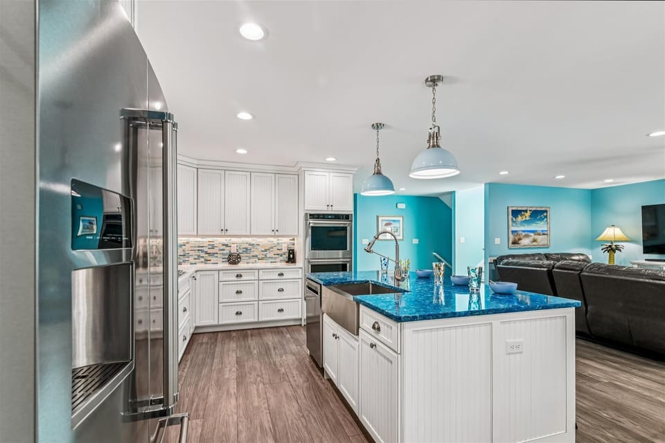 646 Tingle Ave - Gourmet Kitchen Overview - The high-end kitchen boasts white cabinetry, professional stainless steel appliances, and a striking blue-topped center island with a farmhouse sink. Modern pendant lighting hangs over the island, which also provides additional counter seating.