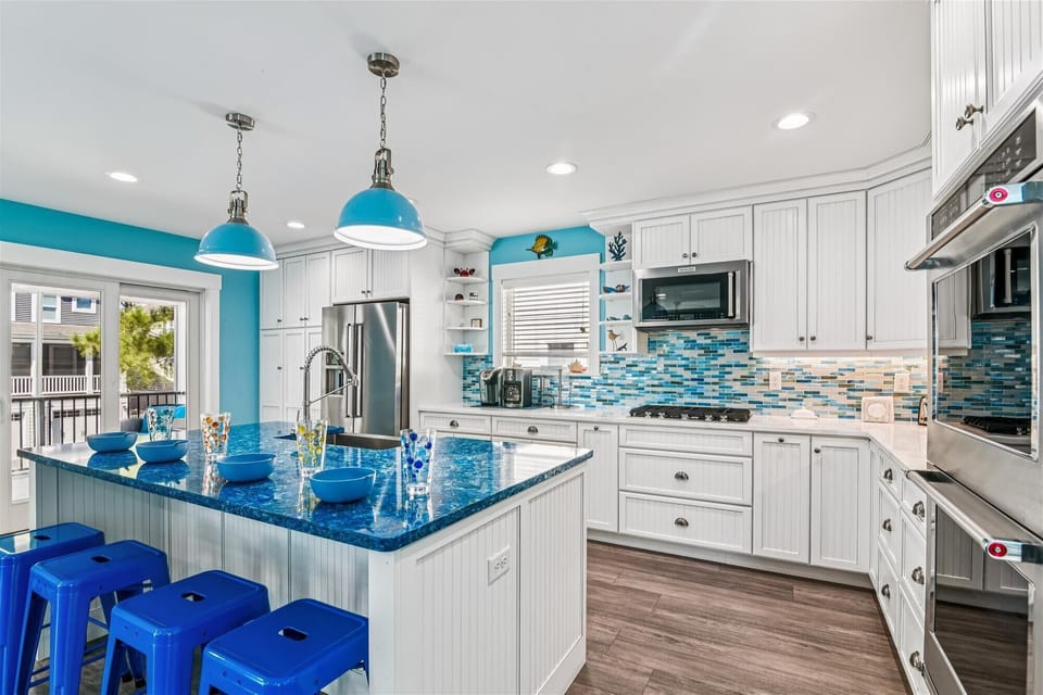 646 Tingle Ave - Kitchen Peninsula and Island - This angle emphasizes the breakfast bar seating at the island, featuring matching blue stools. The kitchen is flooded with light from adjacent windows and glass doors, enhancing the bright, social atmosphere.
