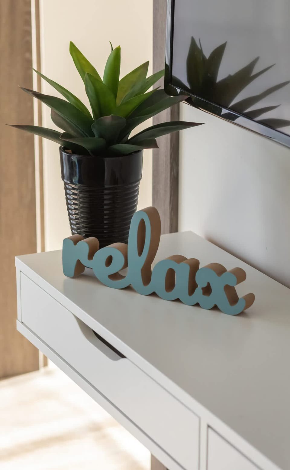 A decorative "Relax" sign with a small plant on a white shelf.

