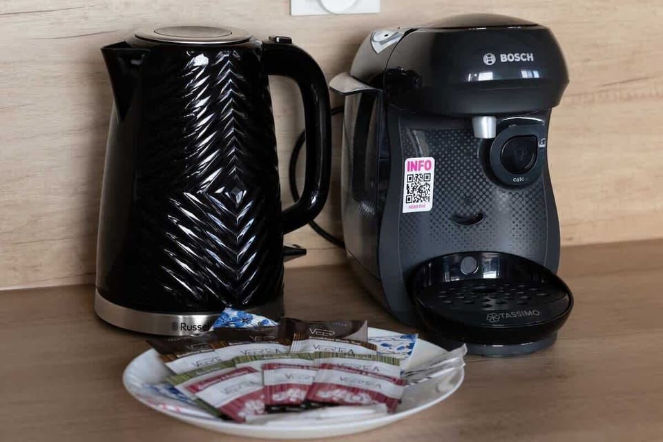 A close-up of a coffee station with a black kettle, coffee maker, and a plate of tea and coffee, offering convenience.
