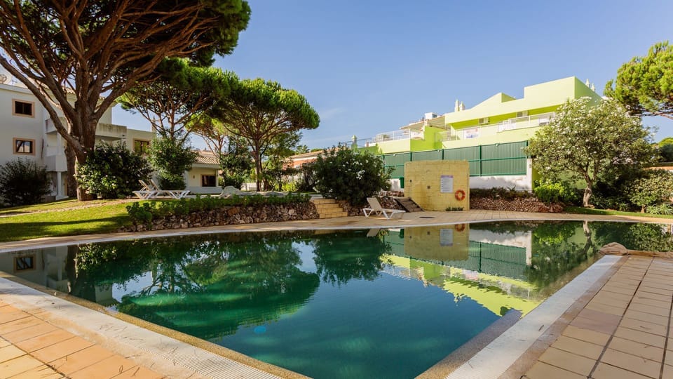 A vibrant green pool invites a refreshing dip under the bright blue sky, surrounded by lush trees providing natural shade.
#PoolArea #OutdoorPool #LovelyStay
