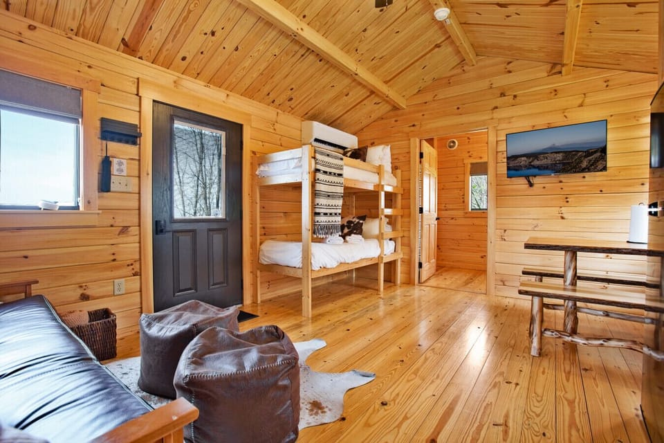 open cabin space with wood bunks, futon, poufs, rustic dining table, and TV
