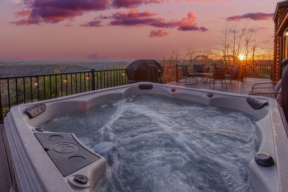 Outdoor hot tub on a deck with patio furniture and grill, overlooking view