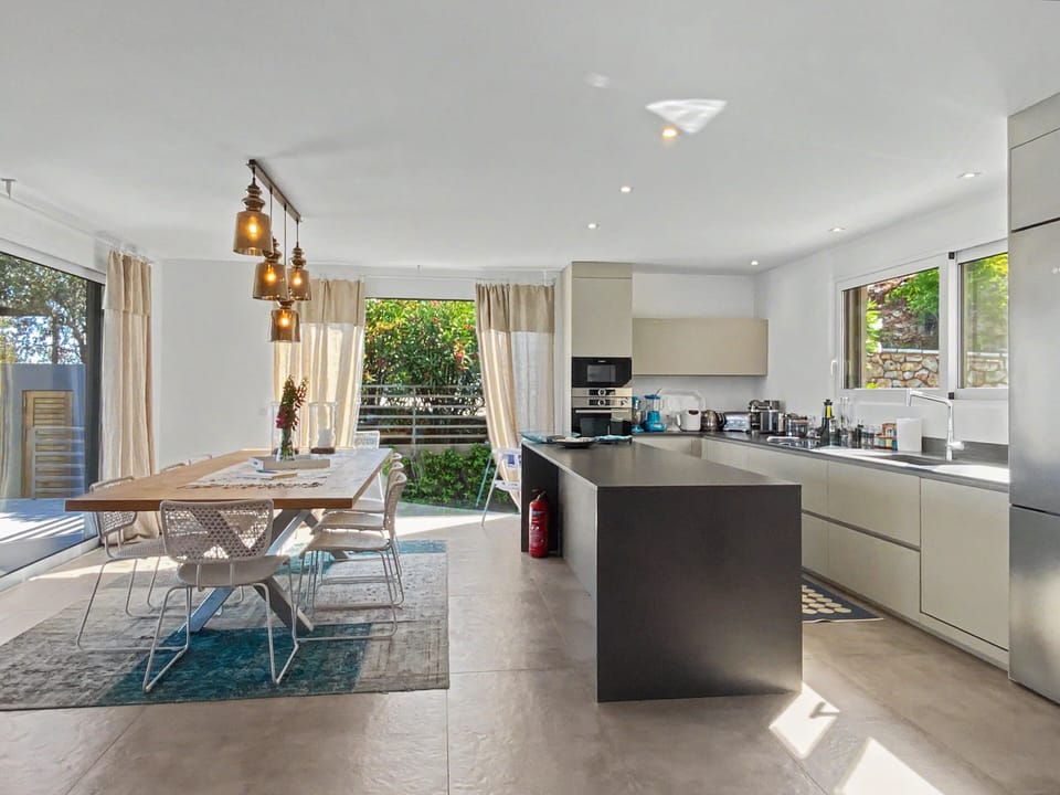 Bright modern kitchen and dining space seamlessly connect to lush outdoor views.