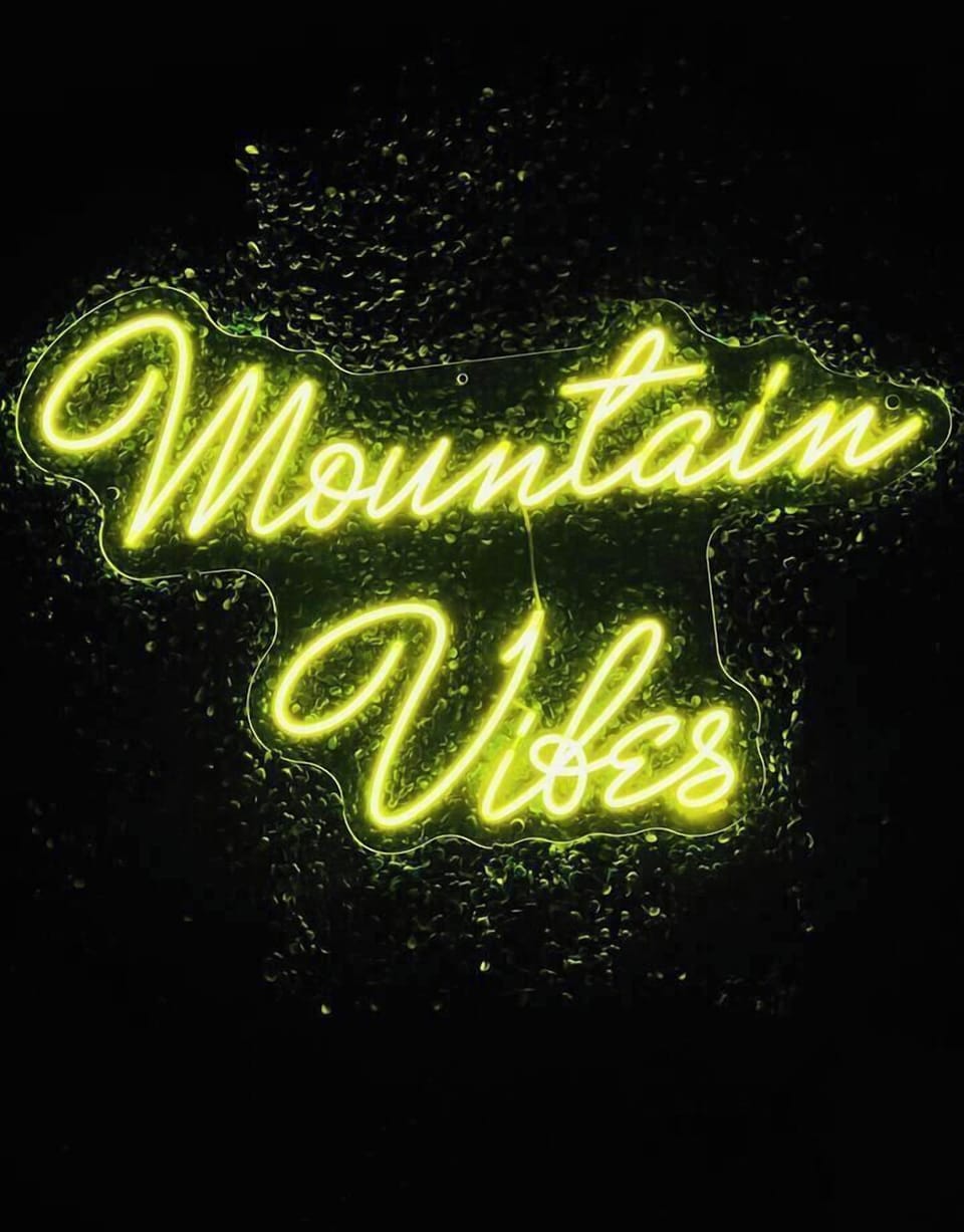 Unwind under the warm glow of our custom "Mountain Vibes" neon sign at night! Located on your private balcony, this hedge photo wall is the perfect backdrop for group vacation memories after a thrilling day of Camelback skiing.