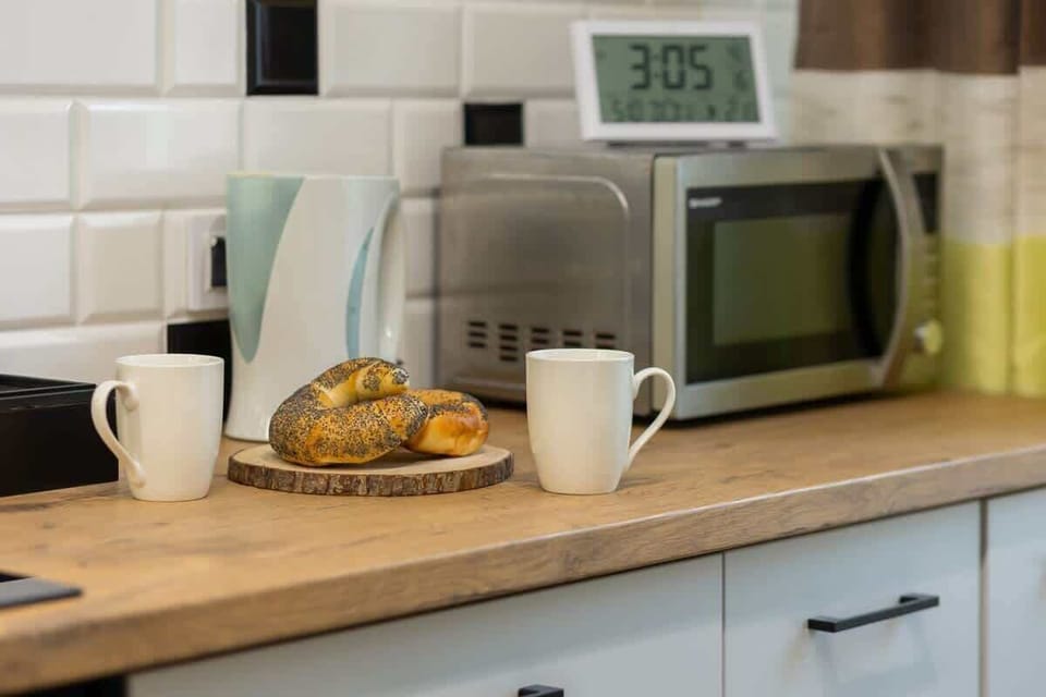 A kitchen countertop featuring a microwave, coffee mugs, and a plate with pastries for a welcoming touch.
