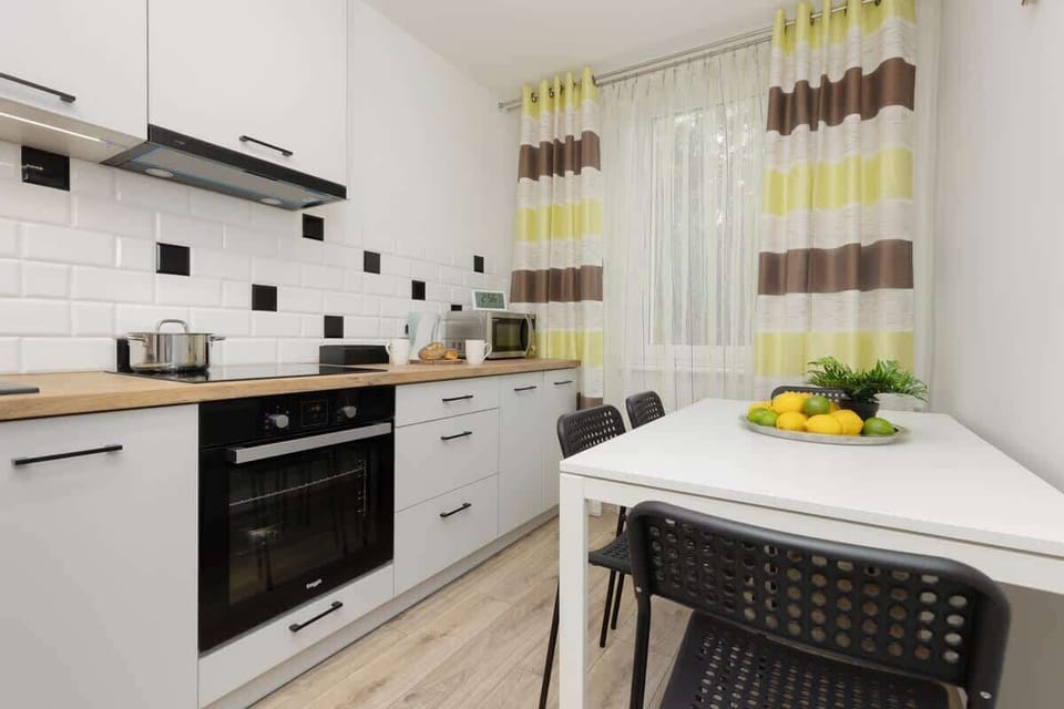 A wide kitchen view, highlighting white cabinetry, a black countertop, and vibrant decor elements like curtains.
