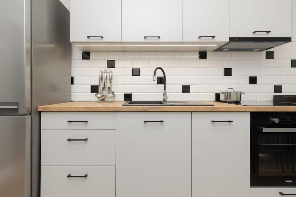 A modern kitchen with white cabinetry, built-in appliances, and a black-and-white tiled backsplash for contrast.
