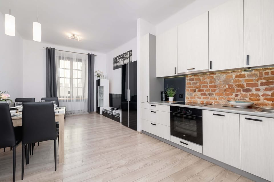 An open-plan kitchen and dining area with a modern white kitchen, wooden flooring, and a dining table for four.
